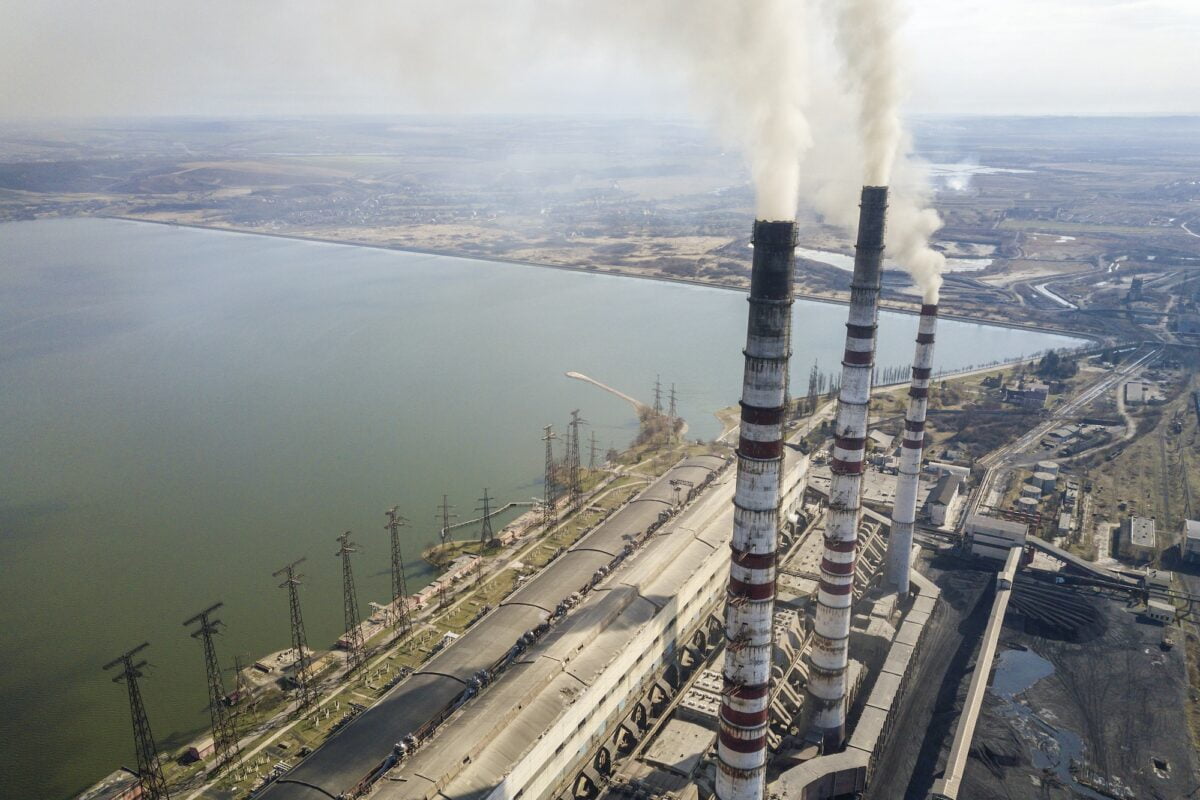 Tall pipes of power plant, white smoke on rural landscape, lake water and blue sky copy space
